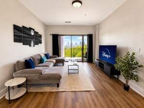 A modern living room with a sectional sofa, a flat-screen TV, a coffee table, and a potted plant. - Executive 3BR Downtown Birmingham with Game Table (Birmingham)