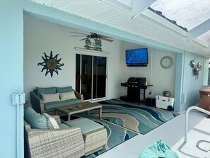 A sunroom with a ceiling fan, a television, a clock, and a grill.