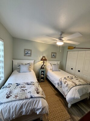 A bedroom with two beds, a ceiling fan, and a small table with a lamp.