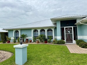 A house with a light blue exterior, a metal roof, and a front porch with potted plants.