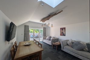 A modern living room with a wooden dining table, a sofa, and a TV mounted on the wall.