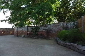 A paved outdoor area with a brick wall, a wooden fence, and a tree providing shade.