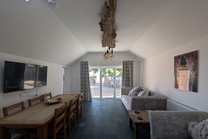 A modern living room with a wooden dining table, sofa, and a large TV mounted on the wall.