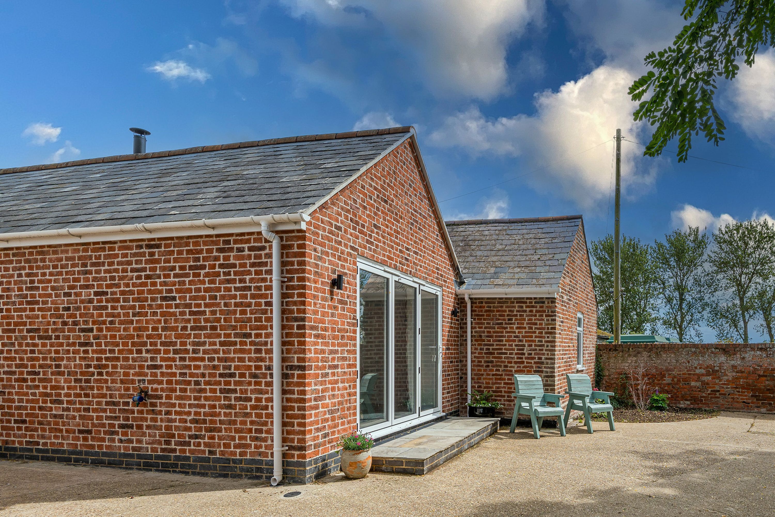 A brick building with a sloped roof, a large sliding glass door, and a small patio area with two chairs.
