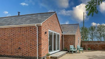 A brick building with a sloped roof, a large sliding glass door, and a small patio area with two chairs.