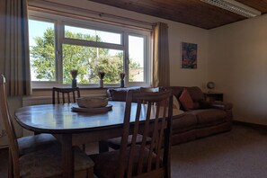 A dining area with a wooden table and chairs, a sofa, and a window with curtains.
