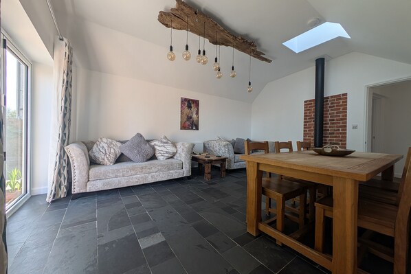 A modern living room with a sofa, dining table, and chairs, a fireplace, and a large window.