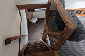 A wooden staircase leading to a room with a grey sofa and a patterned rug.