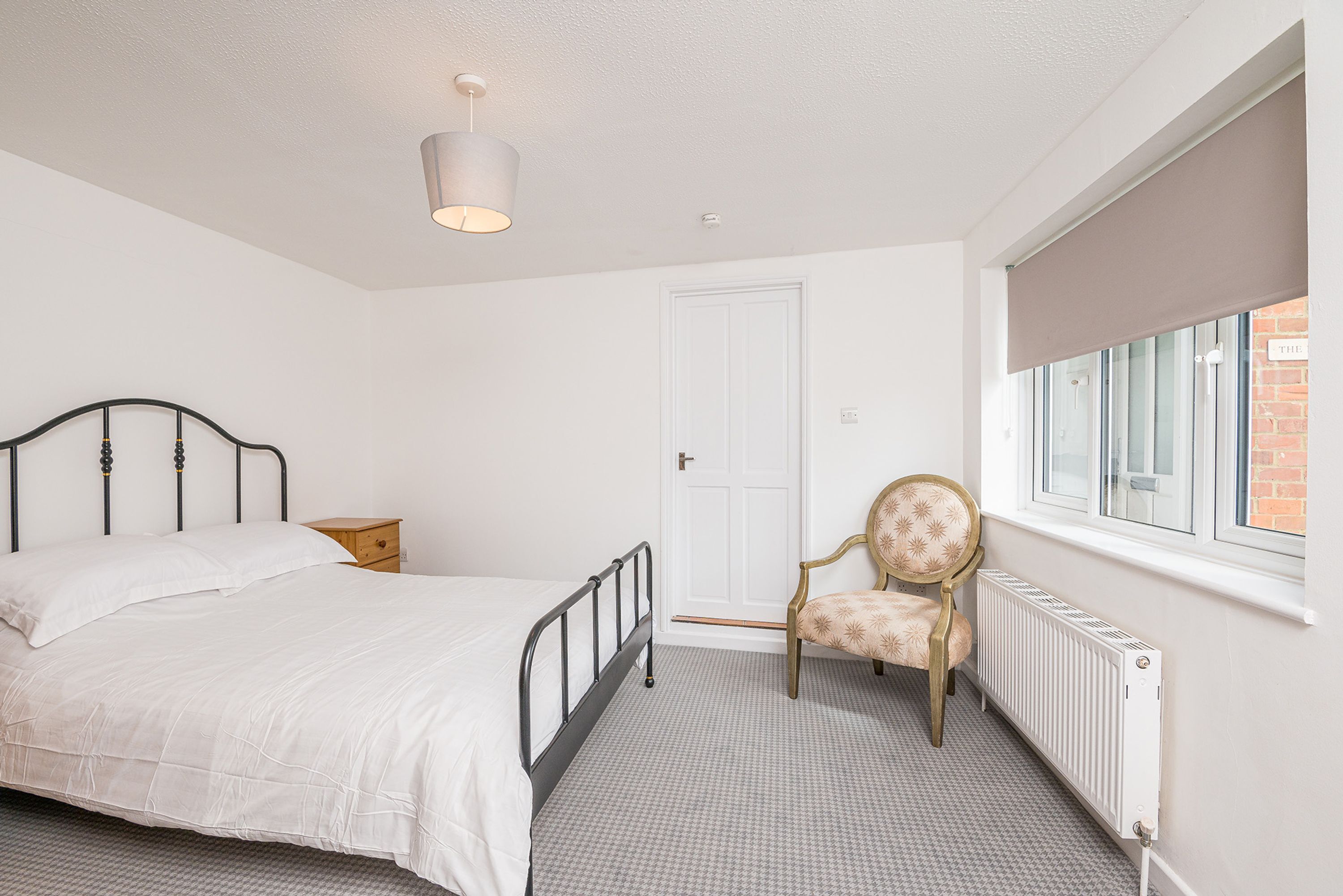 A bedroom with a bed, a chair, a radiator, a window, and a door.