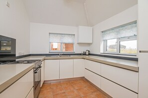 A kitchen with white cabinets, a stove, a sink, and a window with a view of a brick building.
