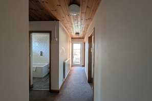 Un pasillo con techo de madera, una bañera blanca y un radiador.