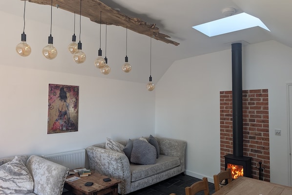 A cozy living room with a sofa, a coffee table, hanging light bulbs, a fireplace, and a skylight.
