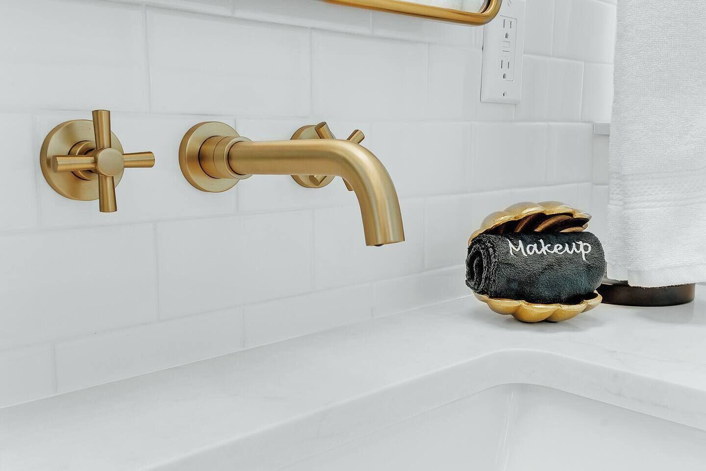 A bathroom with a gold faucet, a towel rack, and a towel with 'Makeup' written on it.