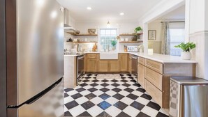 A kitchen with a checkered floor, wooden cabinets, stainless steel appliances, and a window with a plant.
