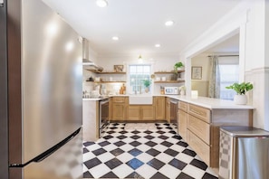 A kitchen with a checkered floor, wooden cabinets, stainless steel appliances, and a window with a plant.