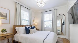 A bedroom with a bed, nightstands, a mirror, and a window with curtains.