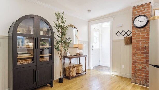 A room with a dark wooden cabinet, a potted plant, wicker baskets, a clock, and a brick wall.