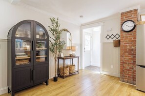 Ein Zimmer mit einem dunklen Holzschrank, einem Blumentopf, Korbwannen, einer Uhr und einer Backsteinwand.