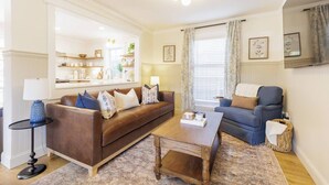 A living room with a brown leather sofa, a blue armchair, a wooden coffee table, and a small side table with a lamp.