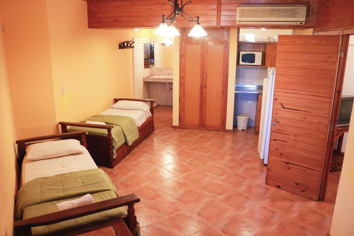 Een compacte kamer met twee bedden, een kleine kitchenette en een badkamer.