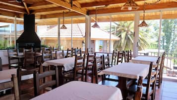 Un restaurant avec des tables et des chaises en bois, une grande cheminée et de grandes fenêtres donnant sur des palmiers.
