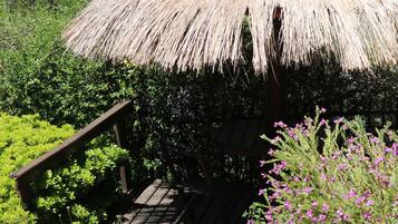 A thatched-roof structure with a wooden deck, surrounded by greenery.