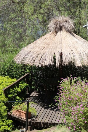 Estructura con techo de paja y terraza de madera, rodeada de vegetación.
