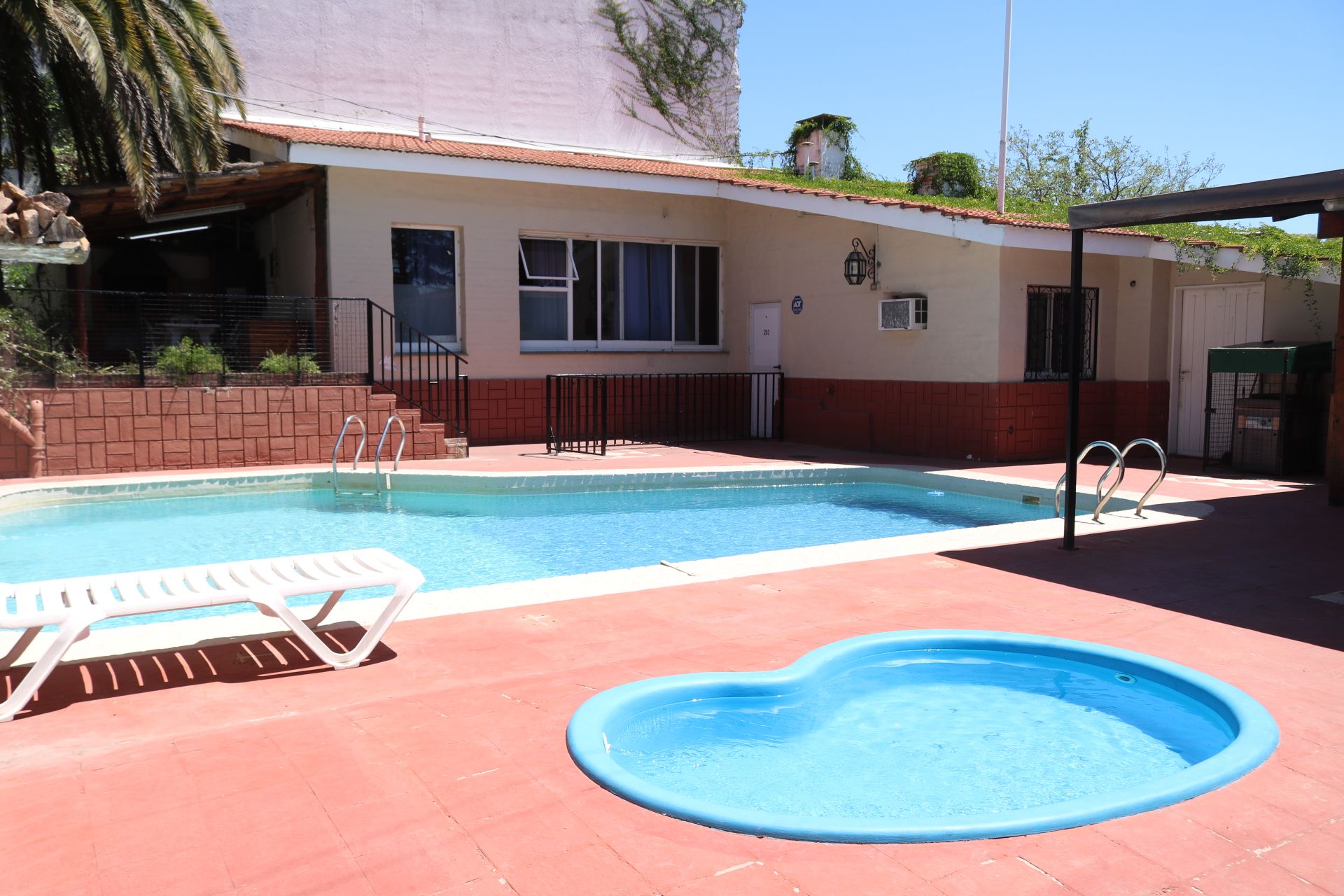 A swimming pool area with a rectangular pool, a smaller heart-shaped pool, and a white lounge chair.