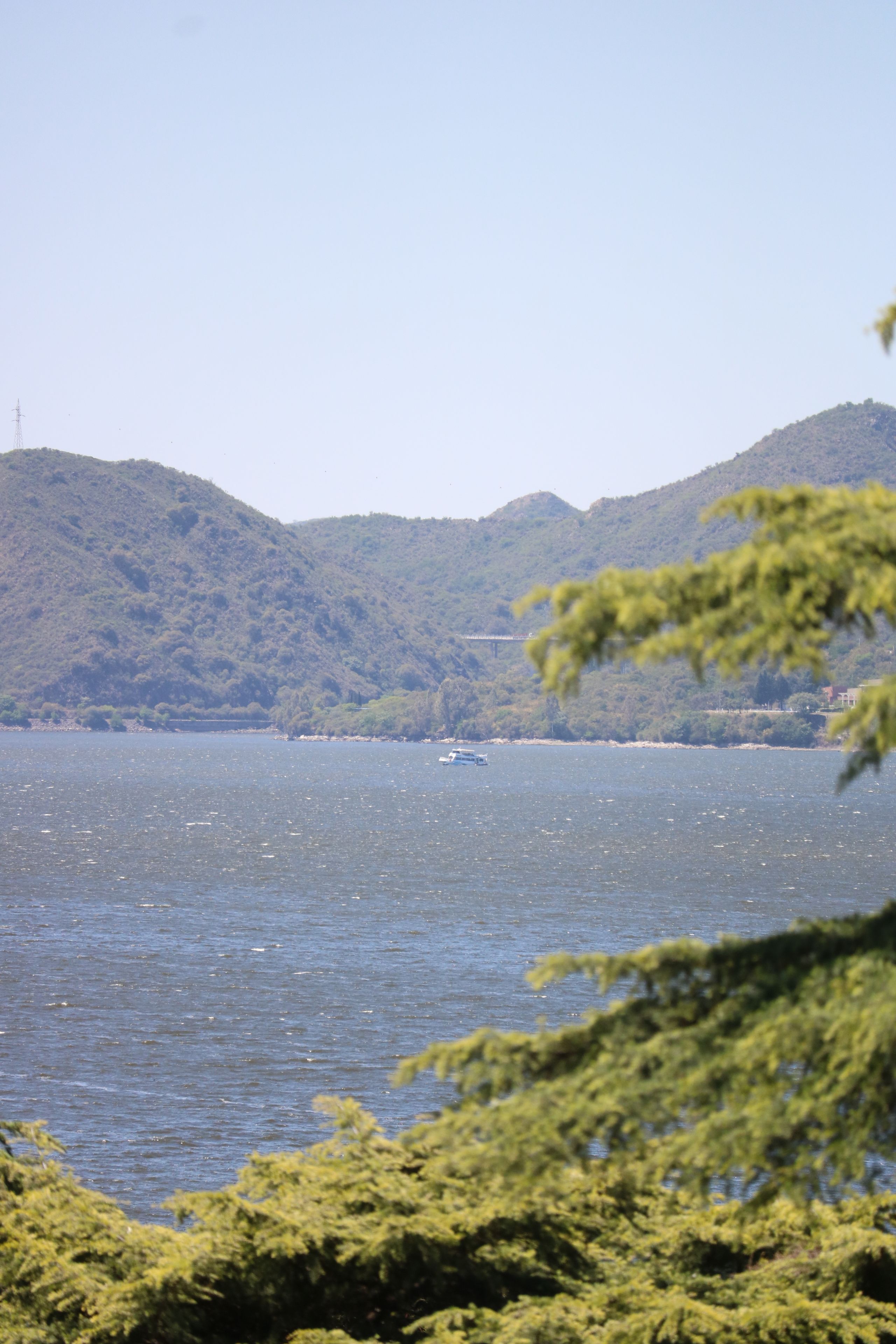 A body of water with a boat, surrounded by hills and greenery.