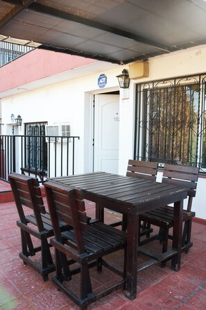 An outdoor patio with a wooden table and benches, a white door, and a window with decorative iron bars.