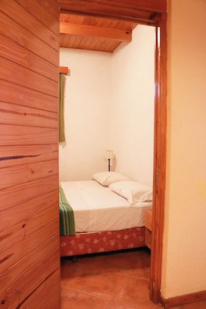 Una habitación pequeña con una cama, una lámpara y techo de madera.