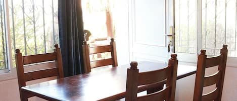 A dining area with a wooden table and chairs, a hanging light fixture, and a window with a view of the outdoors.