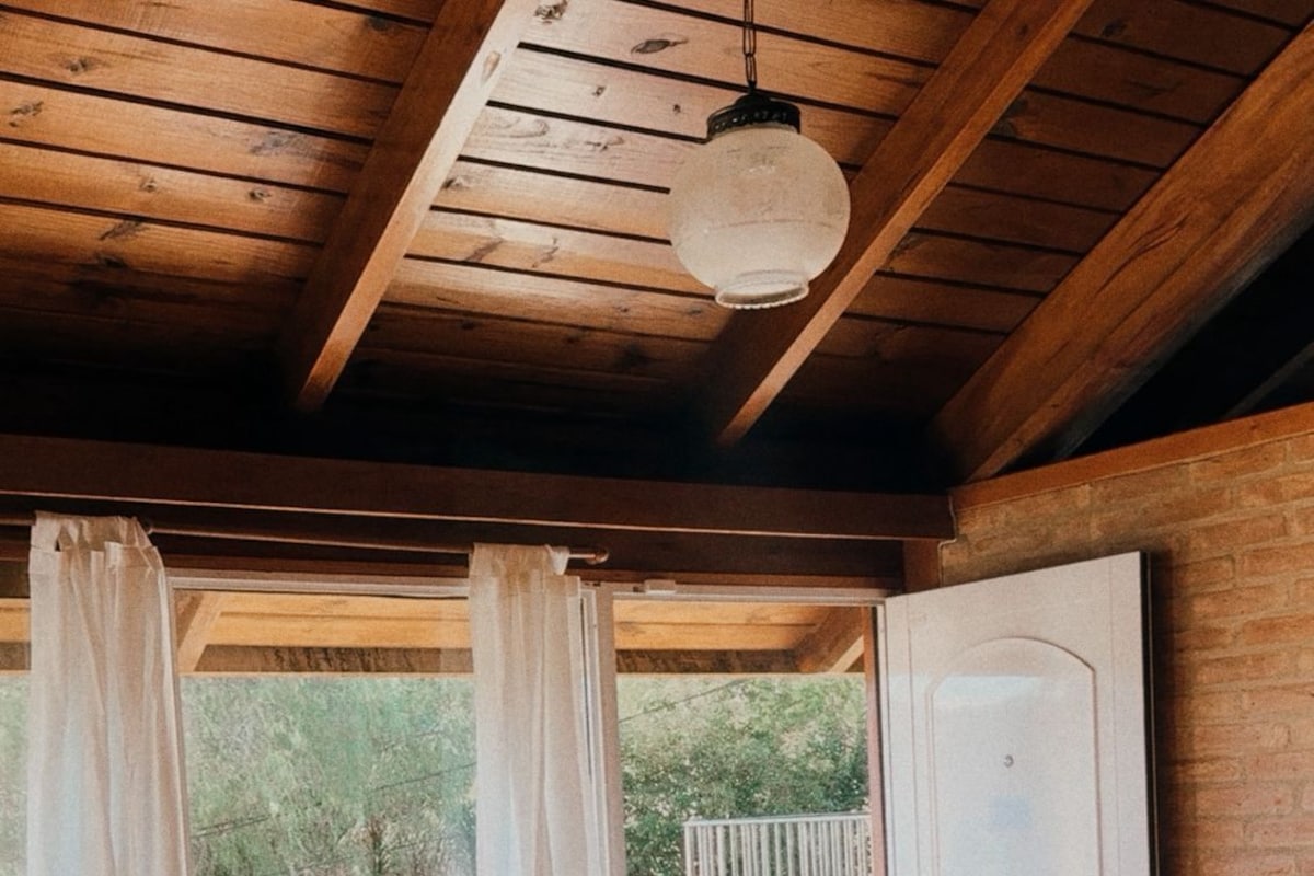 Een kamer met een houten plafond, een bed, een tafel met een stoel en uitzicht op een balkon.