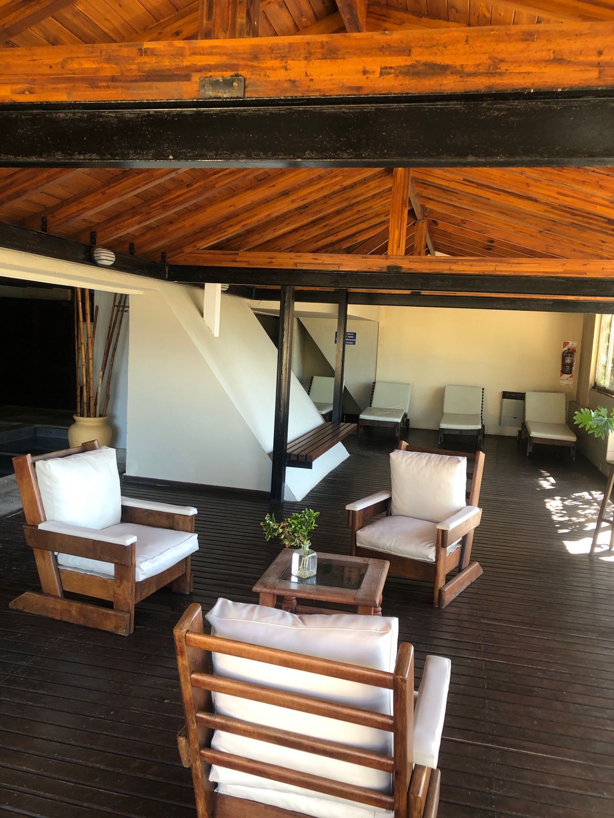 Una terraza de madera con mobiliario exterior, incluyendo sillas y una mesa, y una escalera que conduce a un nivel superior.