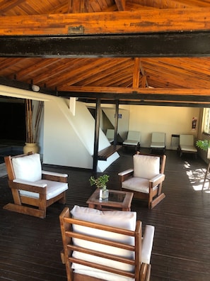 Una terraza de madera con mobiliario exterior, incluyendo sillas y una mesa, y una escalera que conduce a un nivel superior.