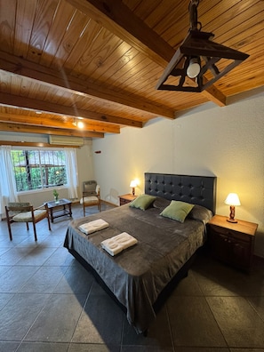Een slaapkamer met een groot bed, twee nachtkastjes met lampen, een raam met gordijnen en een houten plafond.