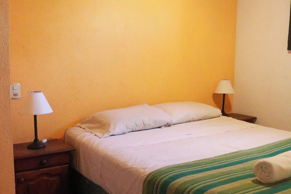 Een slaapkamer met een bed, twee bedlampen, een houten plafond en een betegelde vloer.