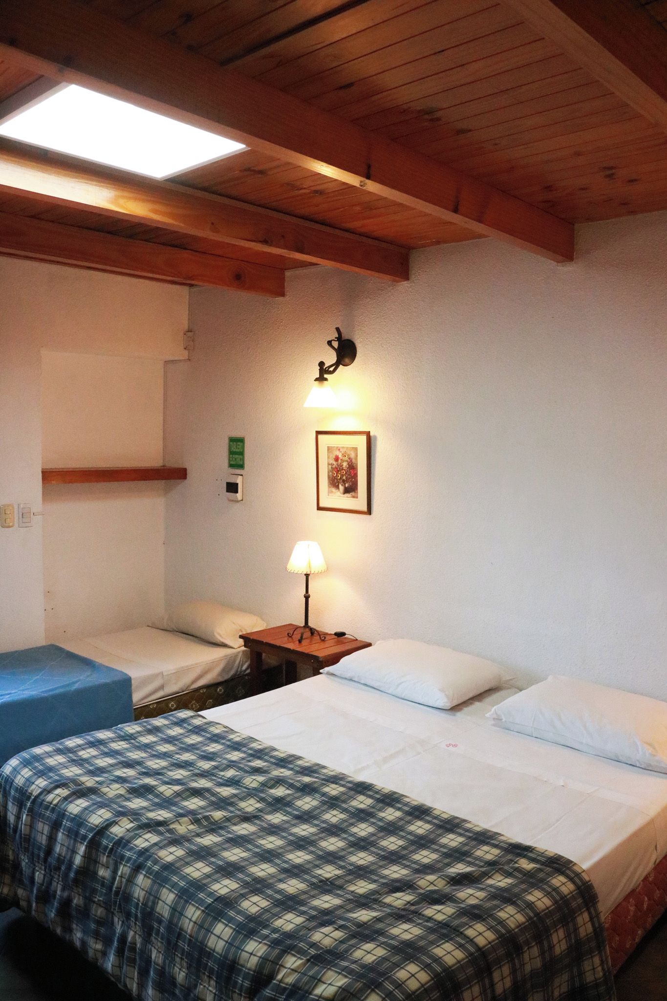 A room with two beds, a wall-mounted light, and a framed picture.