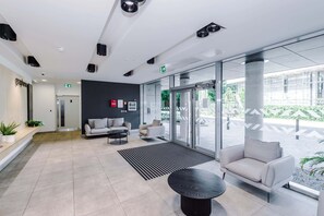 Eine moderne Lobby mit einer Couch, einem Couchtisch, einem Empfangsbereich und einer Glastür, die nach draußen führt.