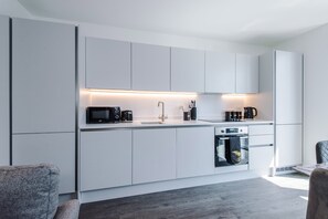 Una cuina moderna amb armaris blancs, forn encastrat i cafetera.