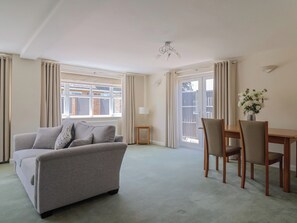 A living room with a sofa, a dining table with chairs, a lamp, and a view through a window. - Frome View (Wareham)