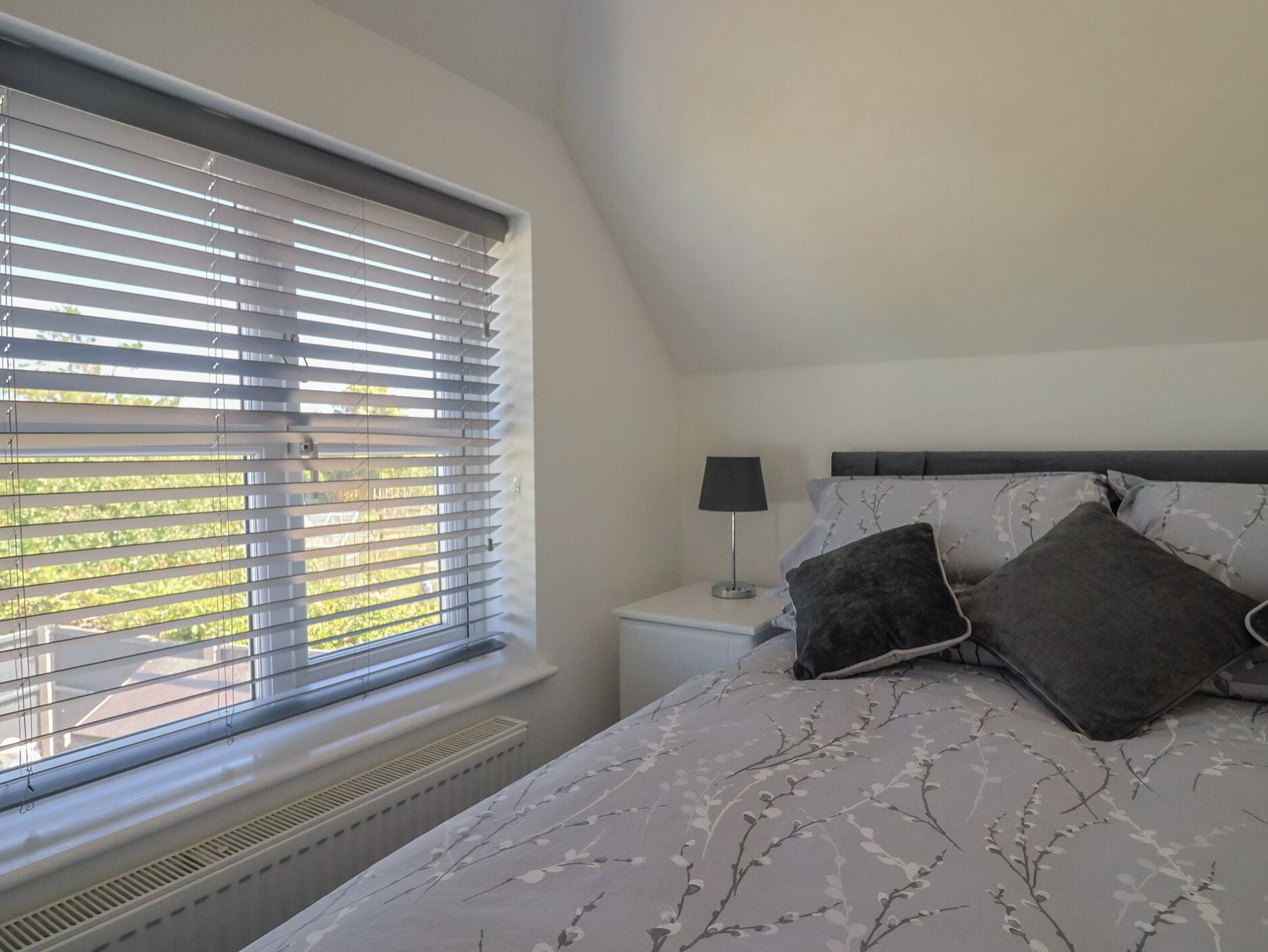 A bedroom with a bed, a nightstand, a lamp, and a window with blinds.