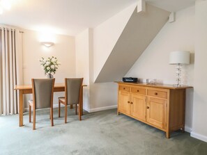 A dining area with a table, chairs, a vase of flowers, a cabinet, and a lamp. - Frome View (Wareham)