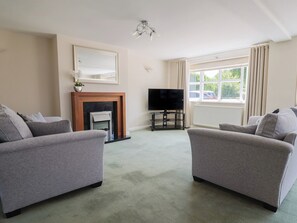 A living room with two grey sofas, a fireplace, a TV on a stand, and a large window with curtains. - Frome View (Wareham)