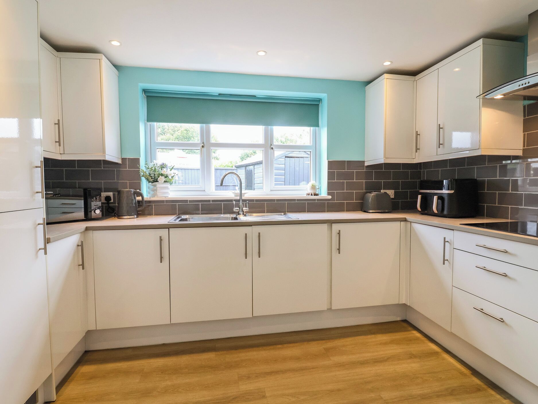 A modern kitchen with white cabinets, a black countertop, and a window with a blue blind.
