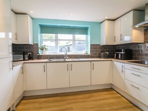 A modern kitchen with white cabinets, a black countertop, and a window with a blue blind. - Frome View (Wareham)