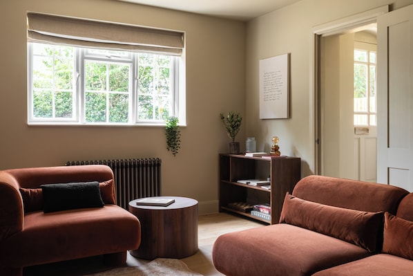 A room with two sofas, a round table, a bookshelf, and a window with a view of greenery.