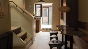 A modern interior with a staircase, a dining area with round tables, and a view through a large window. - Hertfordshire Cottage, Designer, with Barn Suite (Wandon Green)