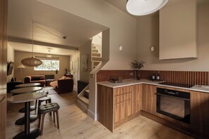 Une cuisine moderne avec des meubles en bois, un four encastré et un coin repas doté de tables rondes et de tabourets.