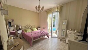 A bedroom with a bed, bedside table, dresser, and a view of the outdoors. - House with a Pool: The Charm of the Pool in Gujan-Mestras (Gujan-Mestras)
